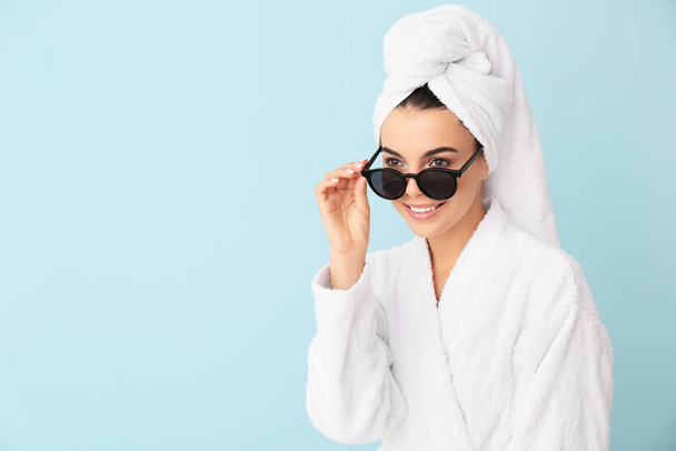 Beautiful young woman in bathrobe and with sunglasses on color background - Fotografie, Obrázek