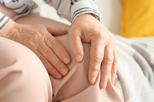 Senior woman suffering from pain in knee at home, closeup - Fotó, kép