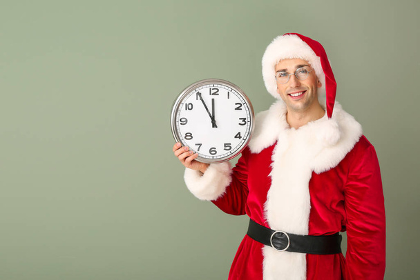 Young man in Santa costume and with clock on color background. Christmas countdown concept - Foto, Imagen