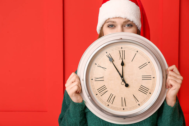 Mujer joven en sombrero de Santa y con reloj sobre fondo de color. Concepto de cuenta atrás de Navidad
 - Foto, imagen
