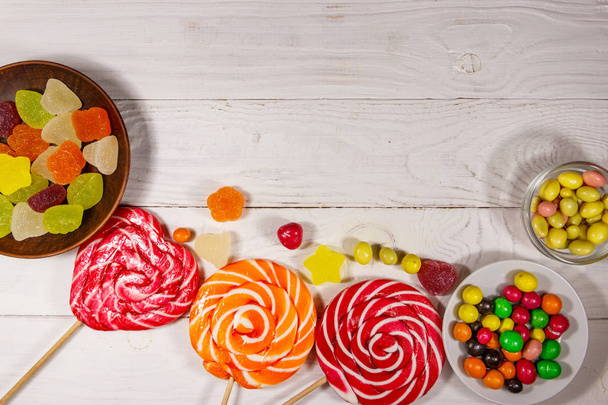 Coloridos caramelos de chocolate, piruletas y dulces de gelatina en la mesa de madera blanca - Foto, Imagen