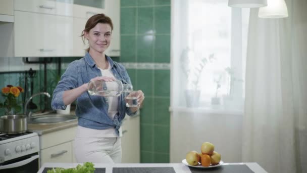 pure water an attractive woman housewife pours glass of drinking liquid it smiles and looks at camera water balance in body - Imágenes, Vídeo