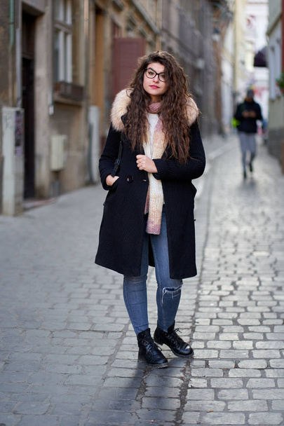 Young woman in black coat and blue jeans in an old town - Foto, afbeelding