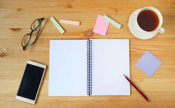 Escritorio con cuaderno abierto blanco, bolígrafo, smartphone, anteojos, papel memo y una taza de té caliente en escritorio de madera
 - Foto, Imagen