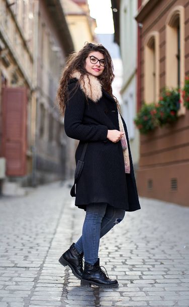 Young woman in black coat and blue jeans in an old town - Φωτογραφία, εικόνα