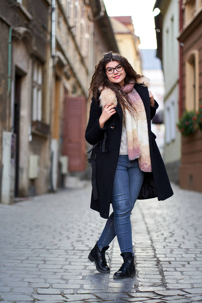 Young woman in black coat and blue jeans in an old town - Photo, Image