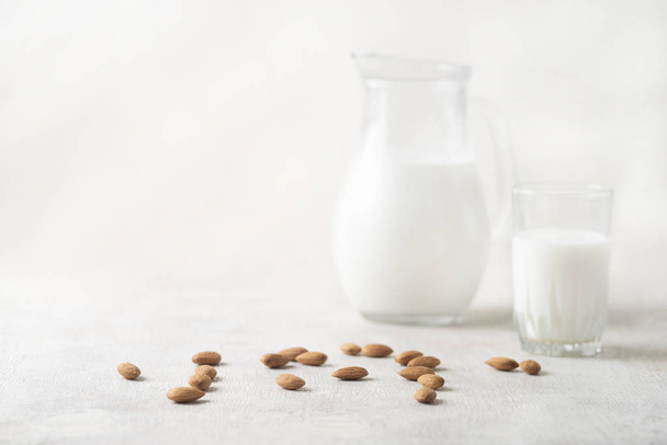 almond and milk in a jug and a glass on a white wooden background.vegan drink.copy space - Фото, изображение