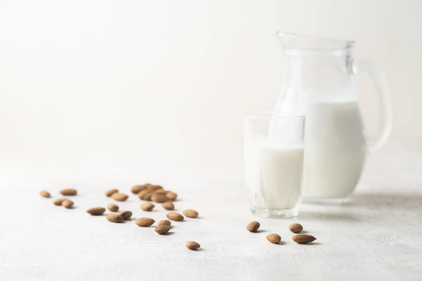 almond and milk in a jug and a glass on a white wooden background.vegan drink.copy space - Фото, изображение