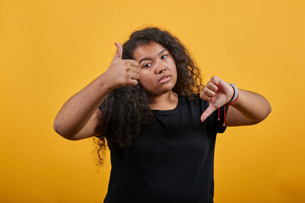 Teleurgesteld krullend afro-Amerikaanse jonge dame wijzen duimen op en neer - Foto, afbeelding