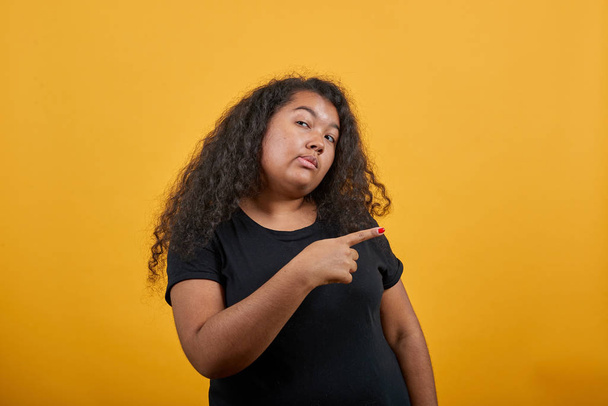 Kudrnatá afro-americká mladá žena ukazuje prstem stranou, dívá se do kamery - Fotografie, Obrázek