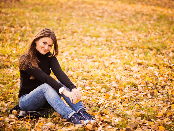 young woman sits on leaves in autumn park - Foto, immagini