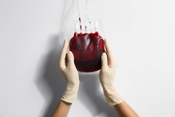 Woman holding blood for transfusion on light background, closeup. Donation concept - Zdjęcie, obraz