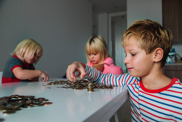kids count money, boy and girls put coins into piggy bank - Foto, afbeelding