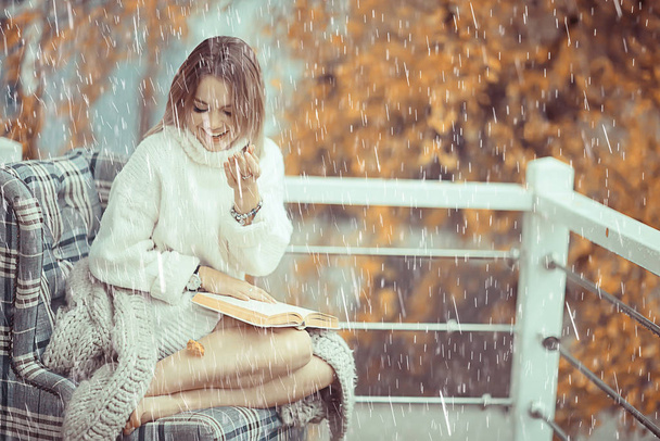 girl with a book in autumn rain on the veranda of the house, seasonal portrait romantic autumn with rain, weather raindrops - Foto, Bild