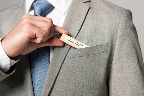 cropped view of businessman putting wooden block with word copyright in pocket isolated on grey - 写真・画像