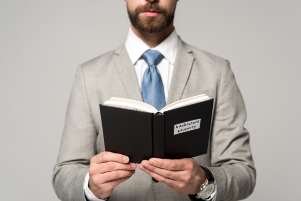 cropped view of businessman reading book with intellectual property title isolated on grey - Photo, Image