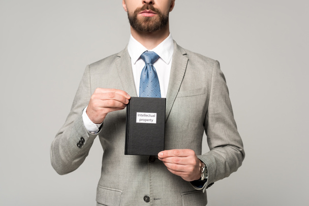 vista ritagliata di uomo d'affari in possesso di libro giuridico con titolo di proprietà intellettuale isolato su grigio
 - Foto, immagini