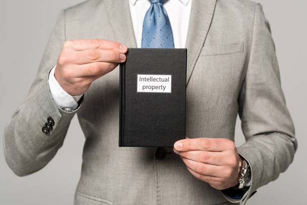 częściowy widok przedsiębiorcy posiadającego książkę prawniczą z tytułem własności intelektualnej odizolowaną na szaro - Zdjęcie, obraz