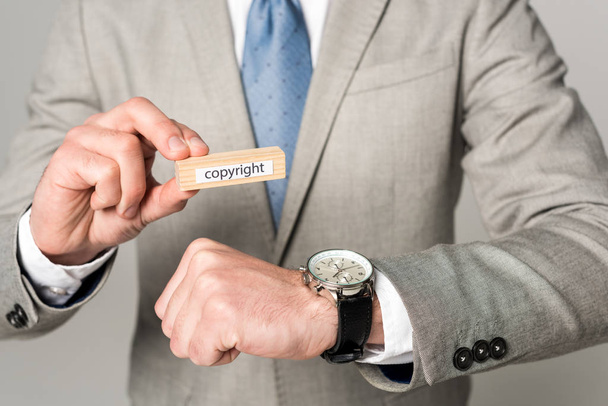 przycięty widok biznesmena w zegarku na rękę trzymającego drewniany blok z napisem praw autorskich odizolowany na szaro - Zdjęcie, obraz