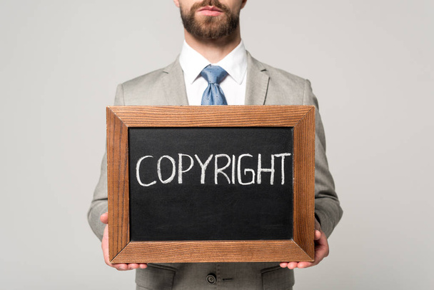 Ausgeschnittene Ansicht eines Geschäftsmannes mit Kreidetafel und Urheberrechtsbeschriftung isoliert auf grau - Foto, Bild