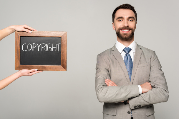 Teilansicht einer Frau mit Kreidetafel mit Urheberrechtsaufschrift in der Nähe eines Geschäftsmannes, der isoliert auf grau in die Kamera lächelt - Foto, Bild