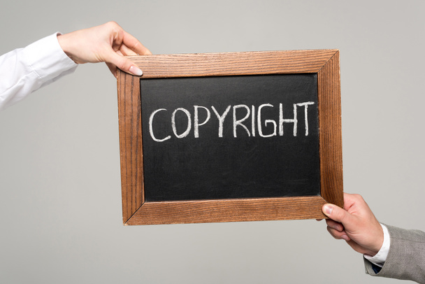 vista cortada de empresários segurando quadro com inscrição de direitos autorais isolado em cinza
 - Foto, Imagem
