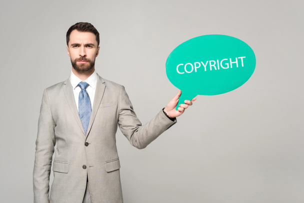 confident businessman holding thought bubble with copyright inscription isolated on grey - Photo, Image