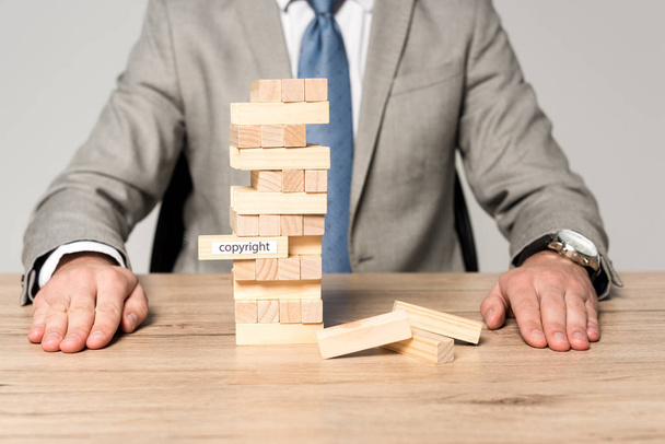 partial view of businessman near blocks wood tower game with copyright inscription isolated on grey - Fotografie, Obrázek