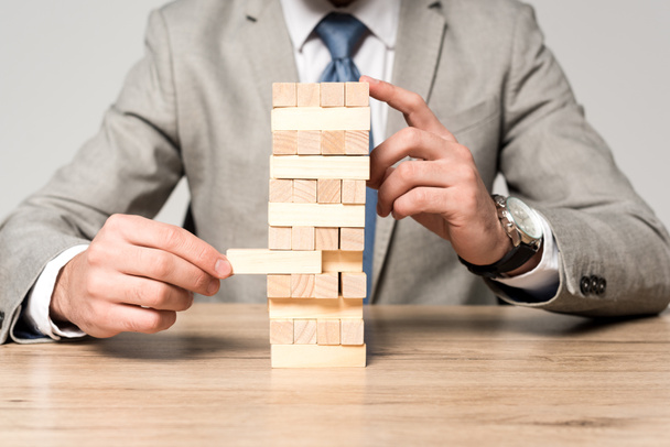 cropped view of businessman playing blocks wood tower game isolated on grey - Foto, immagini