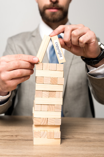partial view of businessman playing blocks wood tower game with copyright inscription isolated on grey - Fotografie, Obrázek