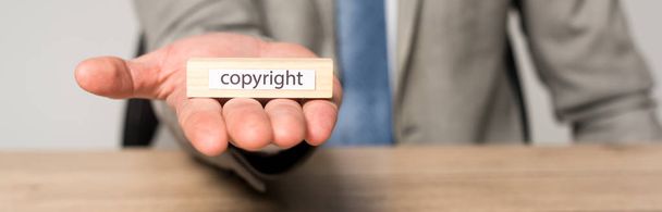 Ausgeschnittene Ansicht eines Geschäftsmannes mit Holzblock mit Urheberrechtsbeschriftung isoliert auf grauem, panoramischem Bild - Foto, Bild
