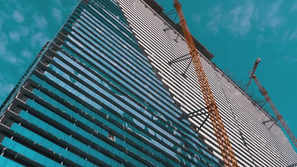 Żuraw na placu budowy przeciwko błękitnemu niebu buduje nowy wieżowiec. Budowa budynku. - Materiał filmowy, wideo
