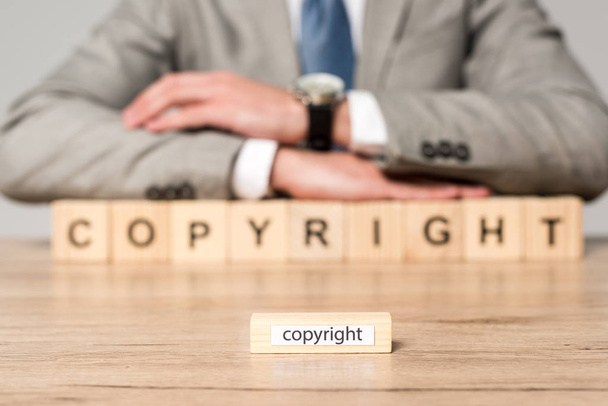 selective focus of wooden block with word copyright, and businessman sitting at desk near wooden cubes with copyright inscription isolated on grey - Photo, Image
