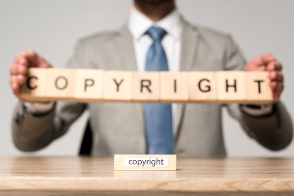 selective focus of wooden block with word copyright near businessman holding wooden cubes with copyright lettering isolated on grey - Foto, imagen