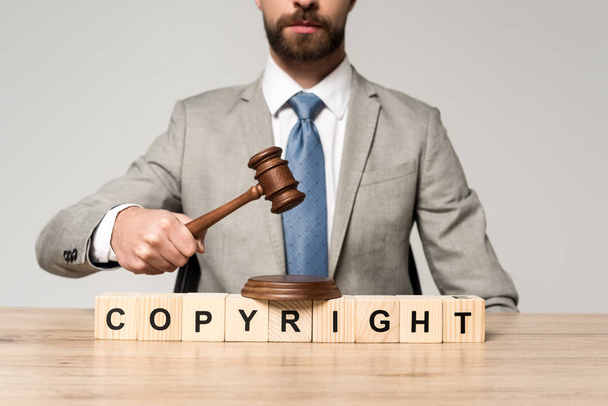 Ausgeschnittene Ansicht eines Richters, der einen Hammer in der Nähe von Holzwürfeln mit Urheberrechtsbeschriftung hält, isoliert auf grau - Foto, Bild