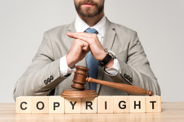 visão parcial de advogado perto de martelo e cubos de madeira com inscrição de direitos autorais isolados em cinza
 - Foto, Imagem