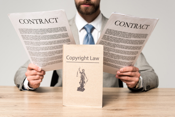 gedeeltelijke weergave van advocaat op zoek naar contracten in de buurt van boek met auteursrecht titel geïsoleerd op grijs - Foto, afbeelding