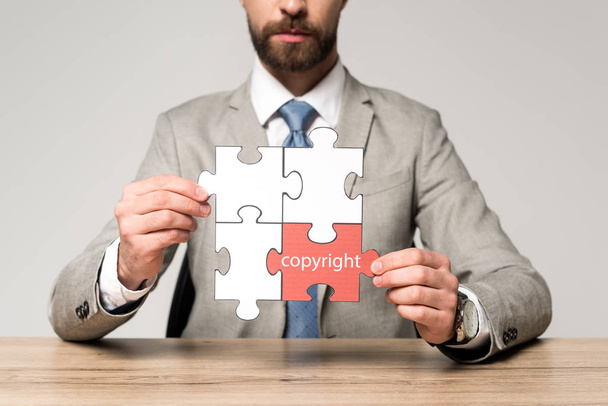 bijgesneden beeld van zakenman met legpuzzel met woord copyright geïsoleerd op grijs - Foto, afbeelding