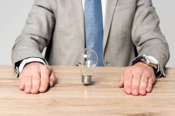 partial view of businessman sitting at desk near light bulb isolated on grey - 写真・画像