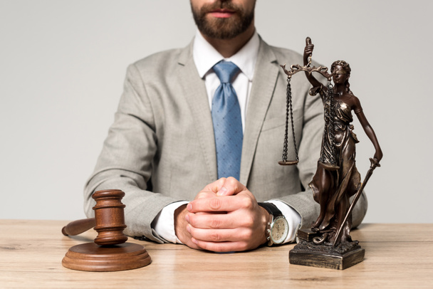 częściowy widok sędziego siedzącego przy biurku w pobliżu młotka i posągu themis odizolowany na szaro - Zdjęcie, obraz