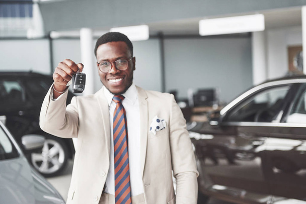 Young black businessman on auto salon background. Car sale and rent concept. - Fotó, kép
