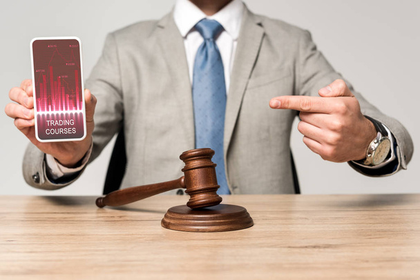 обрізаний вид адвоката, який вказує пальцем на смартфон із додатком торгових курсів, і суддя дав на столі
 - Фото, зображення