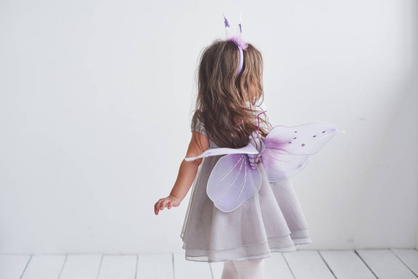 Show your wings. Lovely little girl in the fairy costume standing in room with white background. - Photo, Image