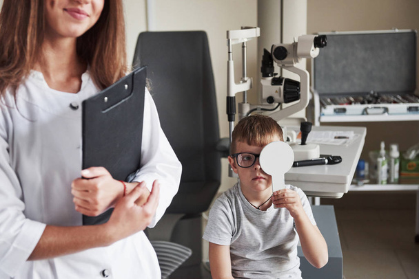 Doing testing in the oculist office with child. Doctor notes data. - Fotoğraf, Görsel