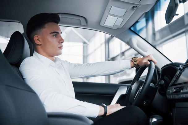 A young man sits in a newly purchased car at the wheel, a successful purchase - Фото, изображение