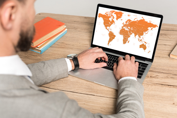 Ausgeschnittene Ansicht eines Geschäftsmannes mit Laptop und Weltkarte auf dem Bildschirm isoliert auf grau - Foto, Bild