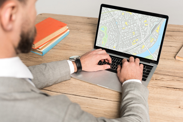 cropped view of businessman using laptop with map on screen isolated on grey - Photo, Image