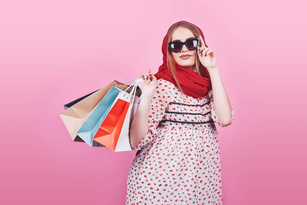 Portrait of young happy smiling woman with shopping bags on the pink Background. - Фото, изображение