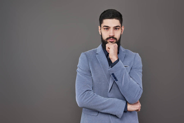 Portrait of freelancer man with beard in jacket standing against gray backdrop. - Zdjęcie, obraz