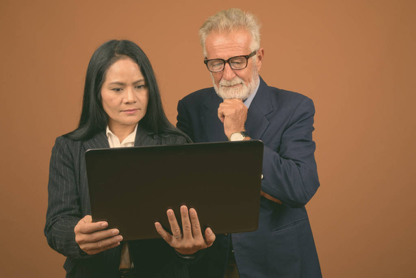 Plan studio d'homme d'affaires senior et femme d'affaires asiatique mature ensemble sur fond brun
 - Photo, image